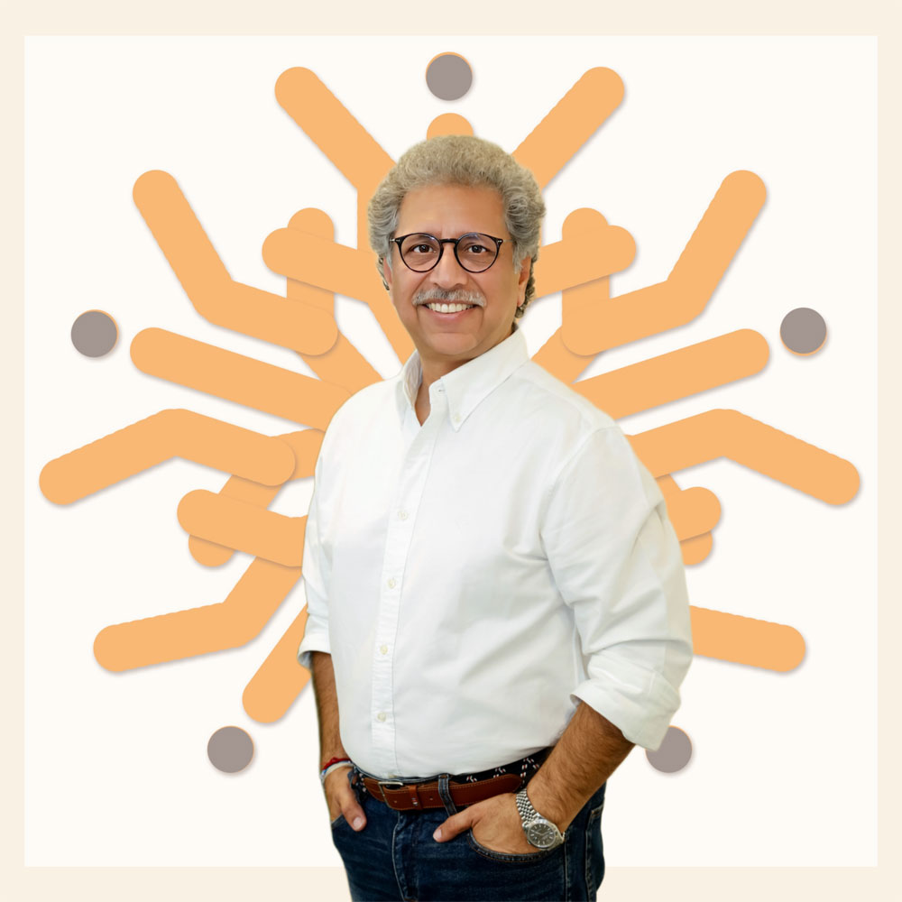 sanjay A man with glasses and a white shirt posing in front of a sunburst design.